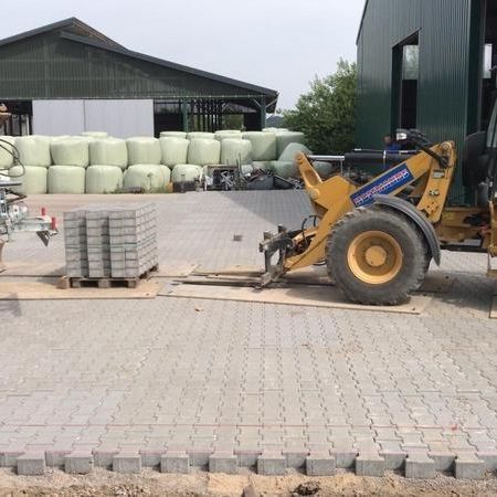 Ein Bagger hebt eine Palette mit Pflastersteinen